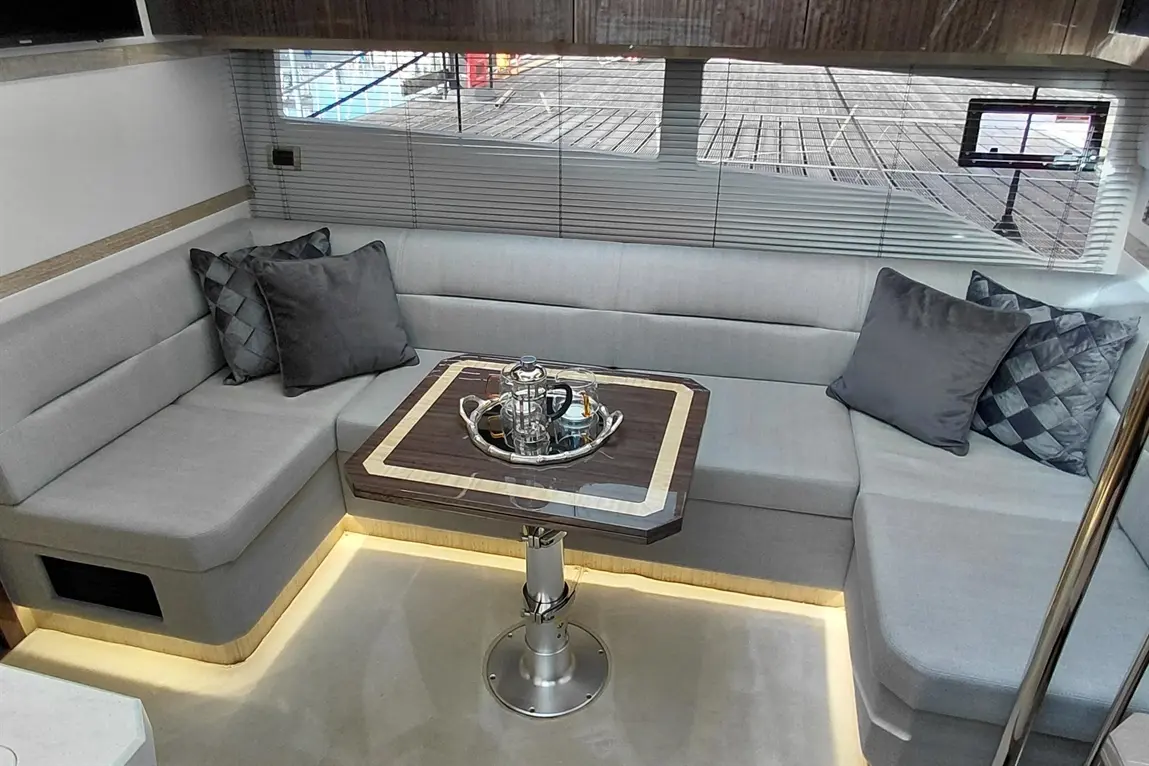 Modern boat interior featuring a grey lounge area, plush cushions, and a stylish table with a tea set, illuminated subtly.